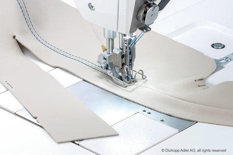 A sewing machine is cutting fabric on the table.