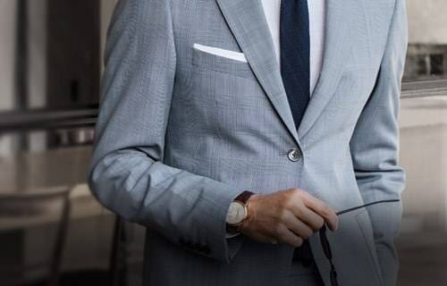 A man in a grey suit adjusting his cufflink.