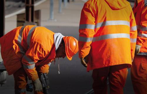 Two construction workers in orange safety gear on a site.